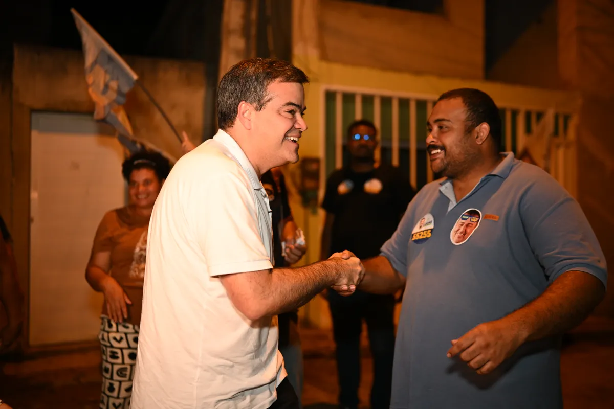 Dr. Lucas 55255 cumprimenta um apoiador na rua, com bandeiras ao fundo