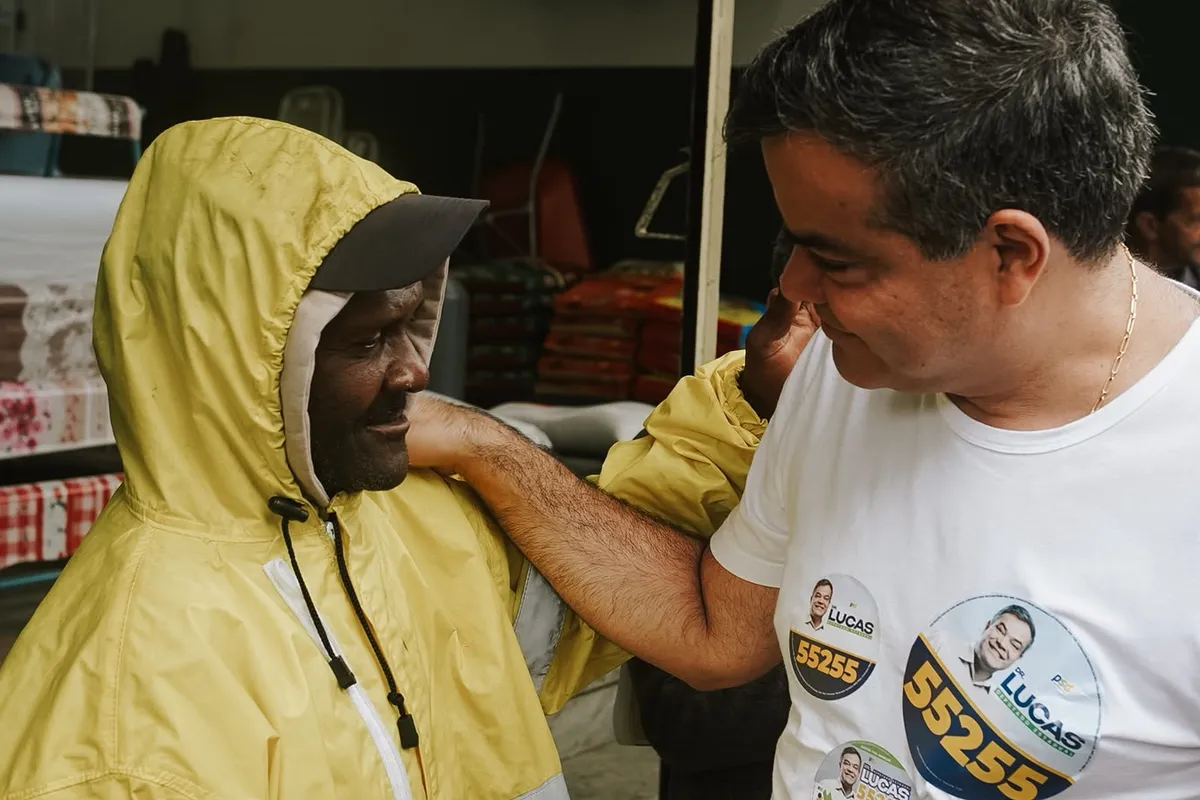 Dr. Lucas 55255 cumprimenta um morador de capa de chuva durante a caminhada em Conceição de Macabu