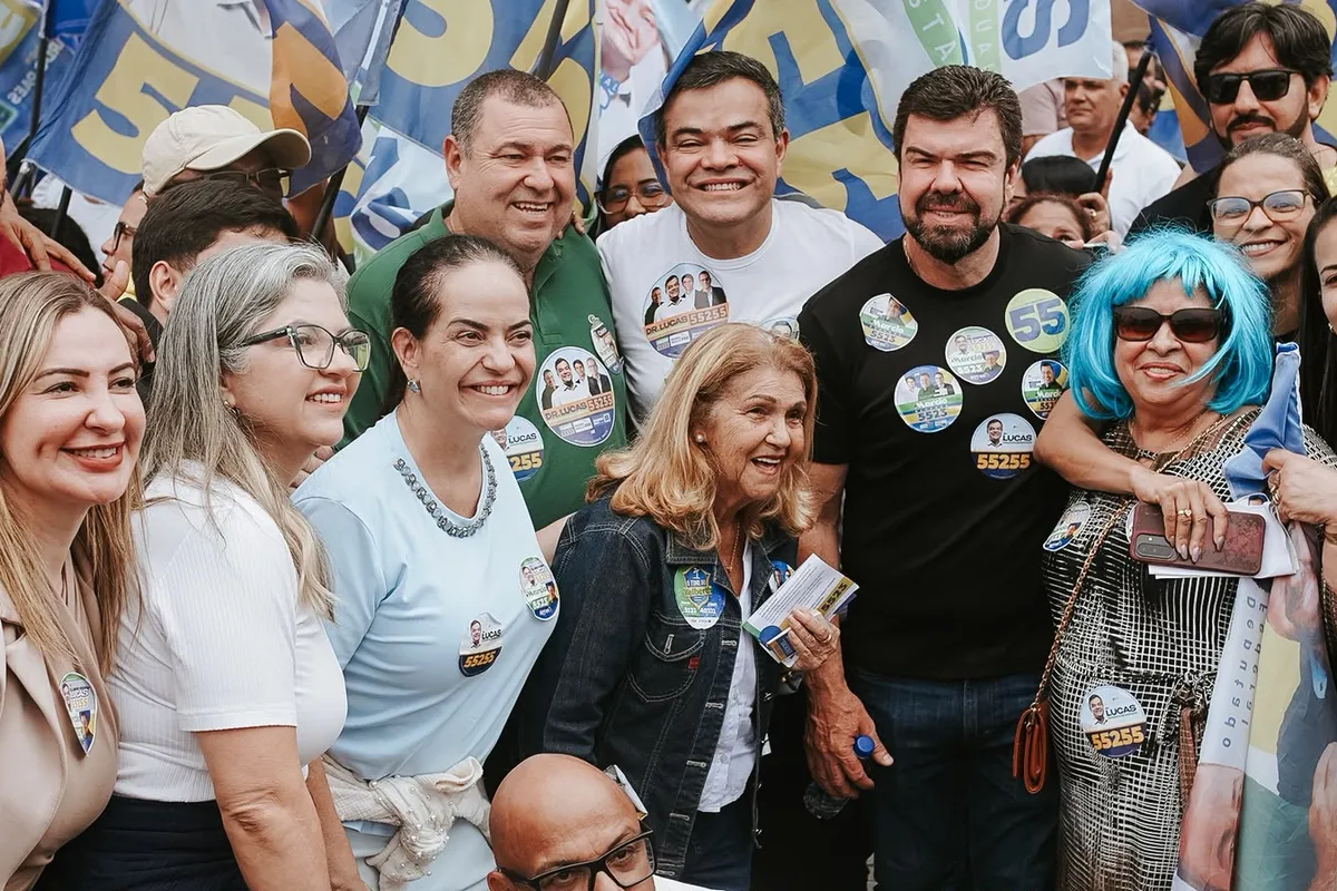 Dr. Lucas 55255 no meio de apoiadoras e lideranças, com as bandeiras da campanha ao fundo, na caminhada em Rio das Ostras